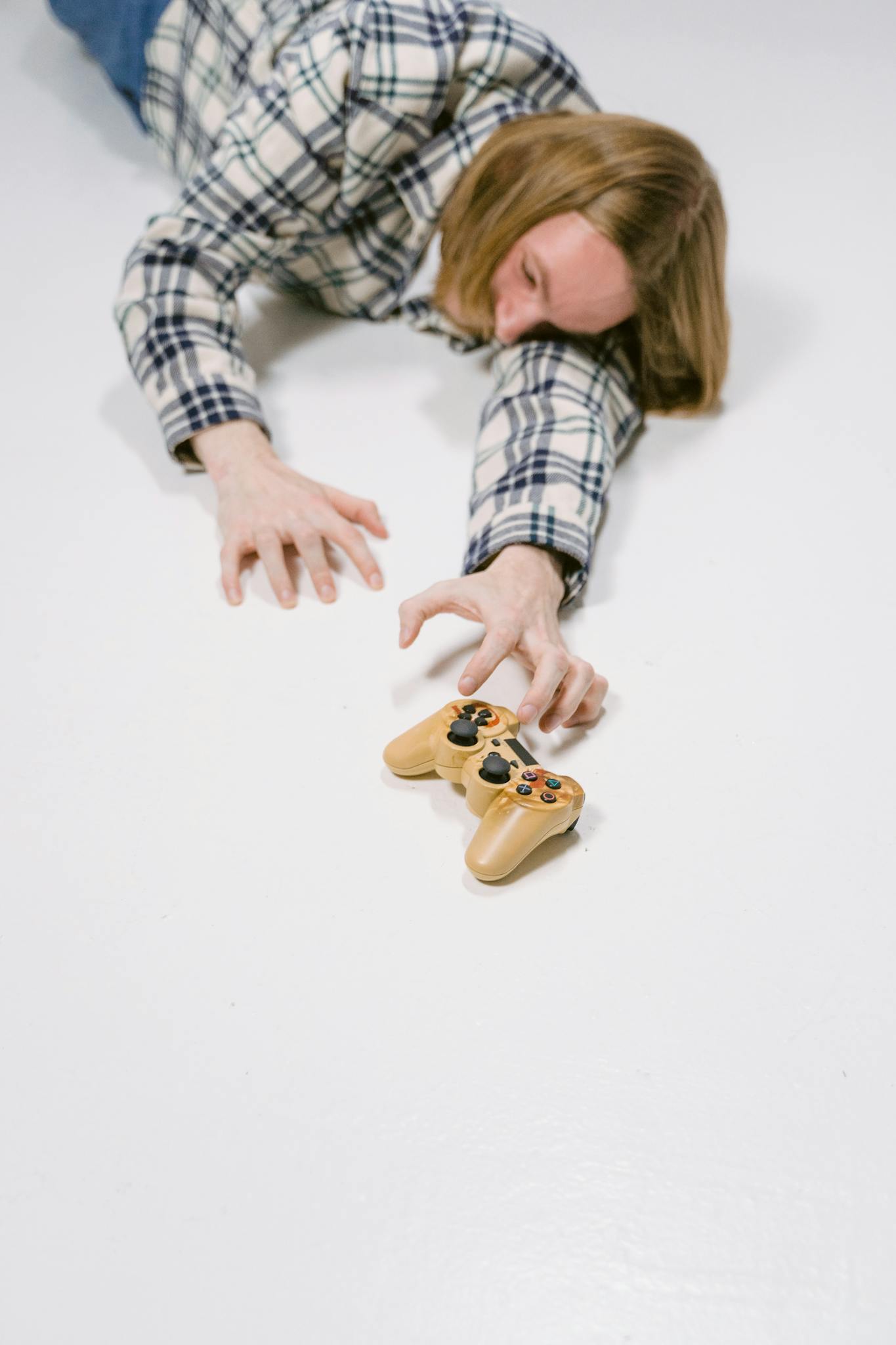 A person lying on a white floor reaching for a game controller, symbolizing gaming passion.